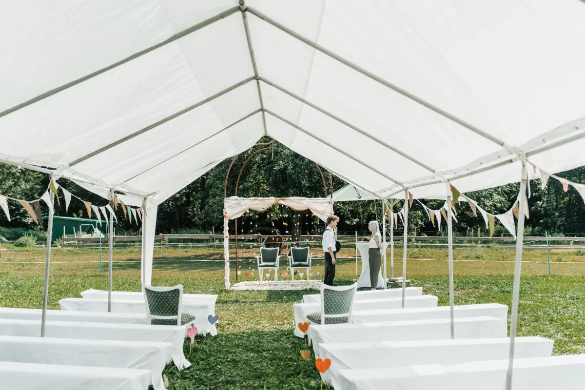Rows of seating set up under a white tent for an outdoor ceremony