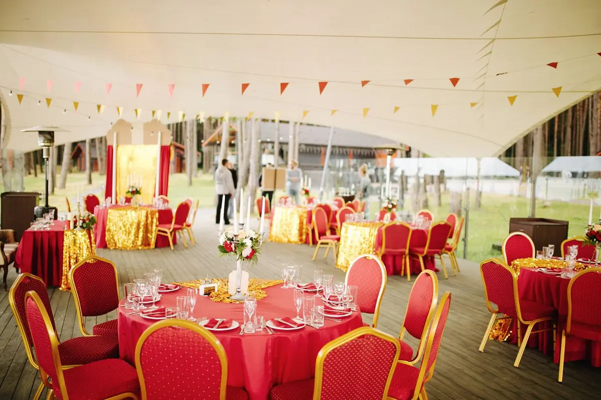 Round tables with red chairs set for a reception under a large white tent