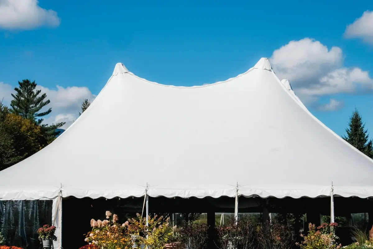 White peak-style event tent set up on a lawn under a blue sky