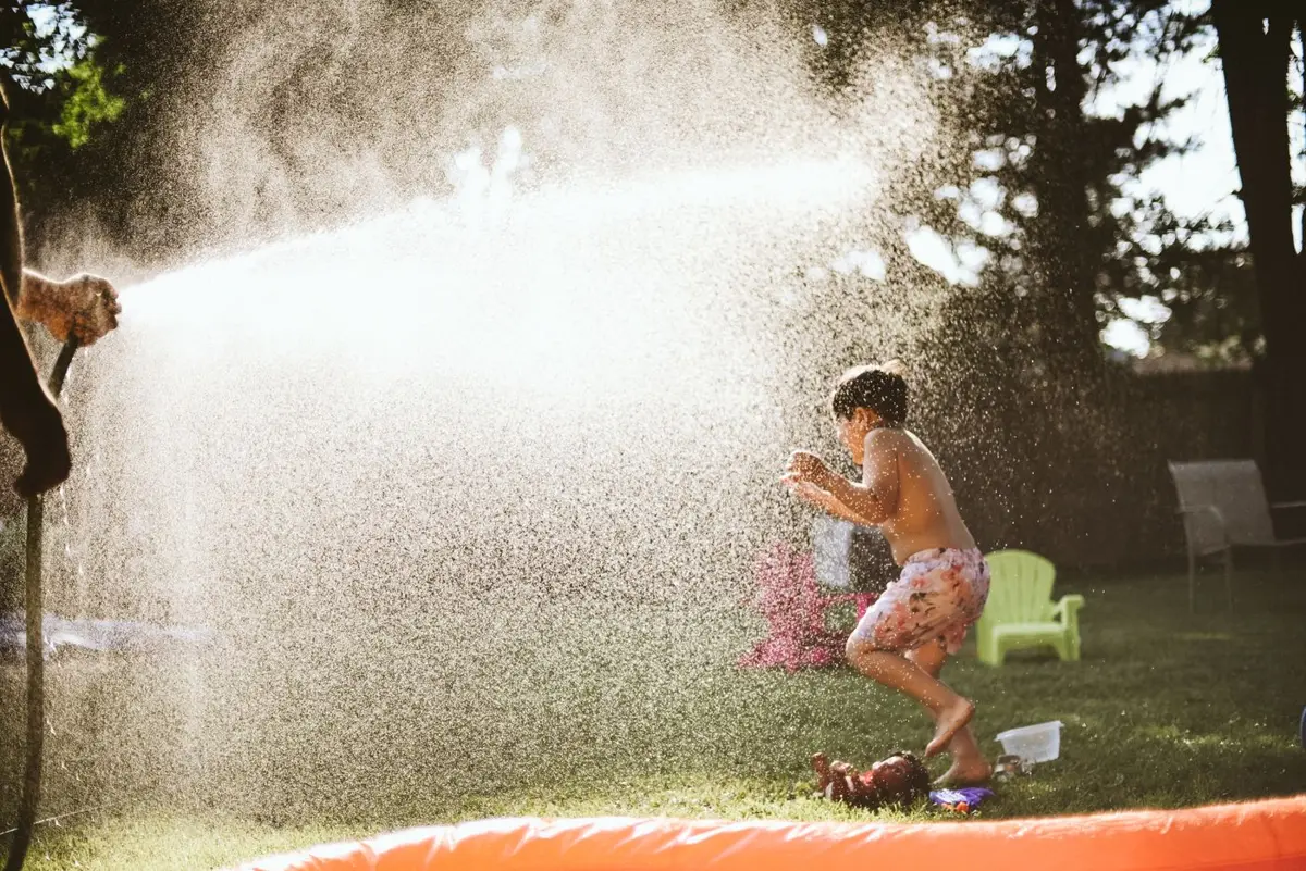 Boy playing in a water spray in a backyard on a hot day