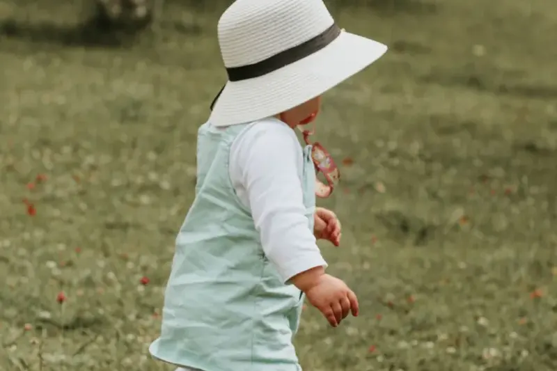Toddler in a sun hat walking on grass