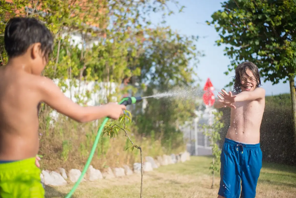 Two boys playing with a garden hose in a sunny backyard